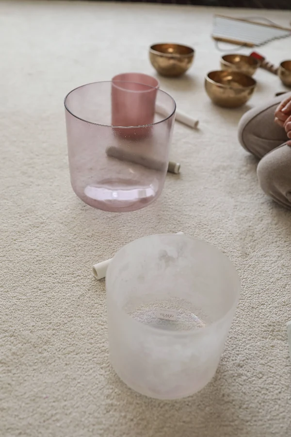 Rosa und weiße Kristallklangschalen mit bronzenen Klangschalen im Hintergrund.